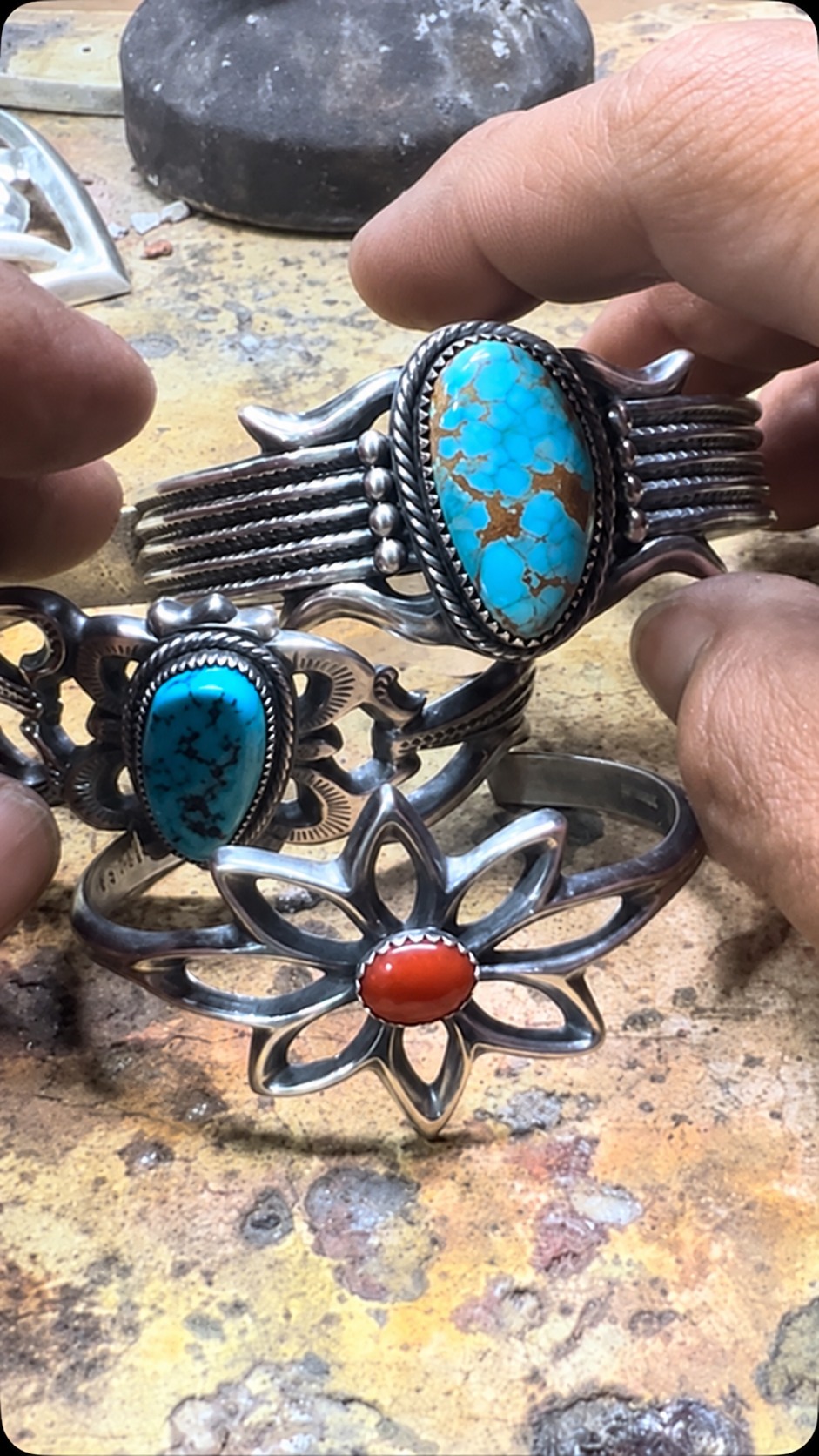 Turquoise and floral cuffs held over the jewelry makers’ workbench